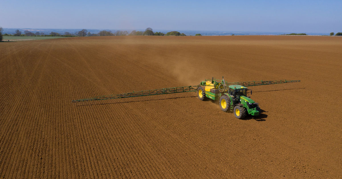 drone shot of a tractor spraying an uncultivated field, aerial view. green and yellow tractors spray grain on the brown soil. a vast, empty plain in the background.