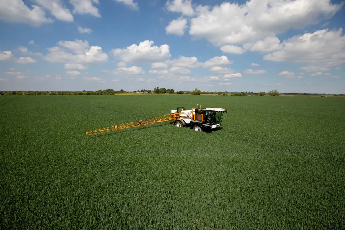 Agricultural sprayer working across a green crop